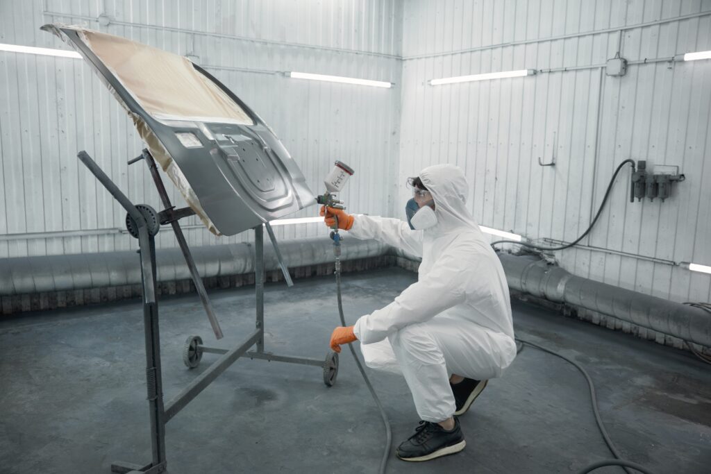A technician spray-painting the bonnet of a car inside a booth.