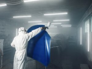 Industrial automotive spray painting Worker spray painting a blue automotive part in a paint booth.